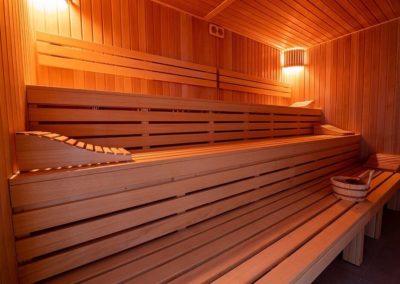 Wnętrze saunarium, widać trzy drewniane ławy, po bokach świecą się lampy.