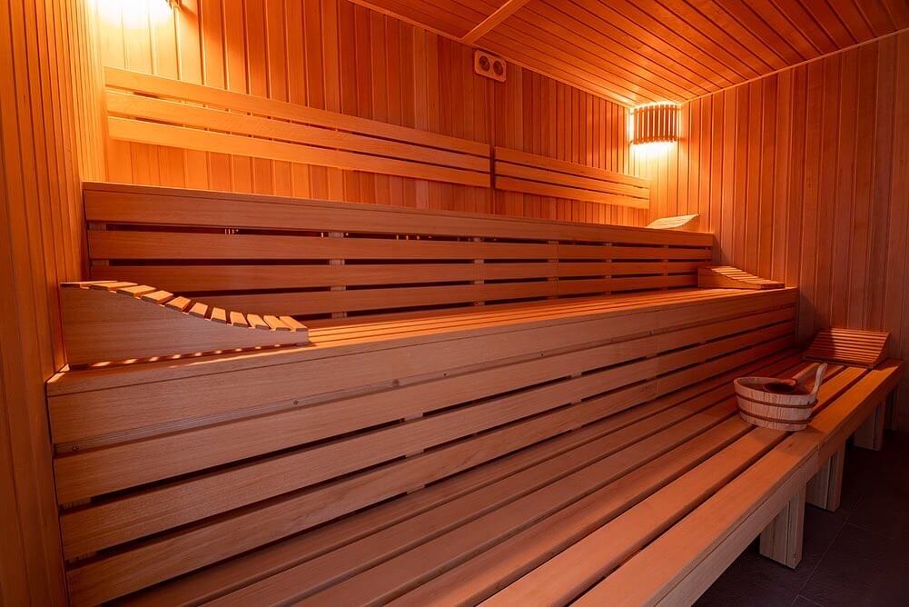 Wnętrze saunarium, widać trzy drewniane ławy, po bokach świecą się lampy.