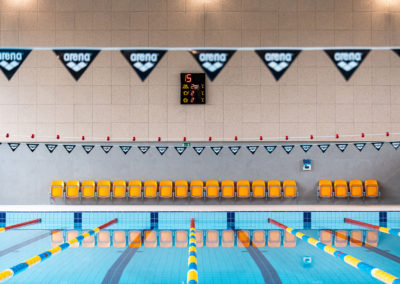 Widok na miejsca siedzące ustawione pod ścianą pływalni przeznaczone dla trenerów i instruktorów