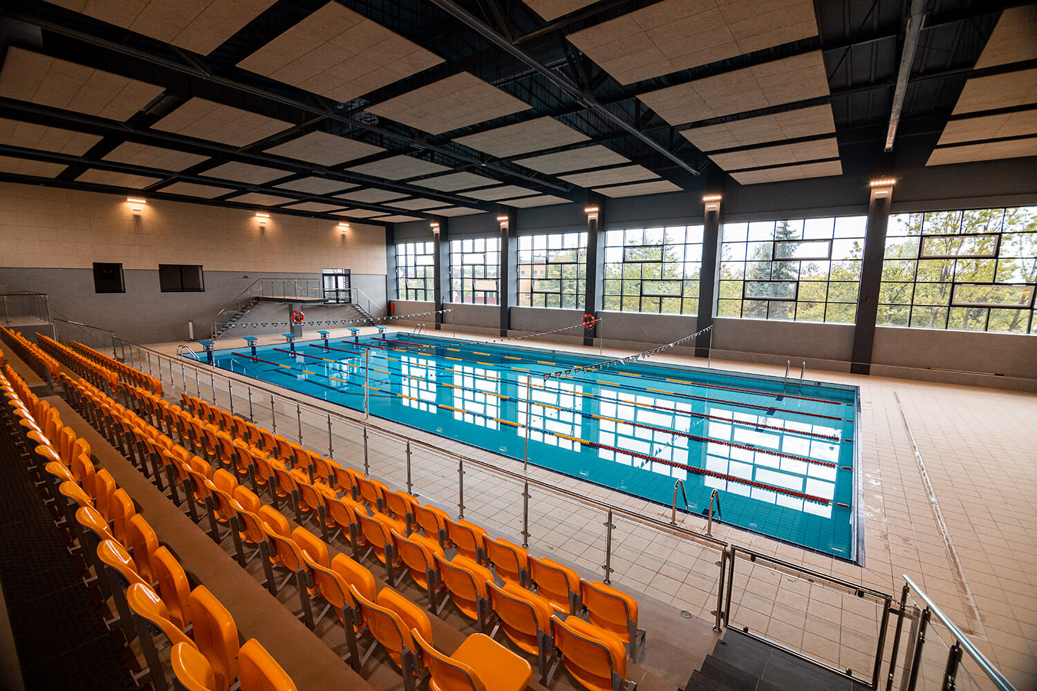 Widok wnętrza basenu: sześć torów pływackich oraz miejsca dla widowni po lewej stronie obiektu. Naprzeciwko widać okna obiektu.