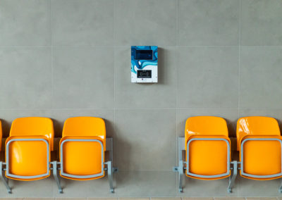 Na ścianie wisi czytnik do zegarków ESOK (Elektronicznego Systemu Obsługi Klienta), poniżej po obu stronach stoją złożone krzesełka.