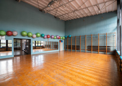 Sala gimnastyczna wyposażona w drabinki, wysokie lustra na ścianach oraz duże piłki do ćwiczeń.
